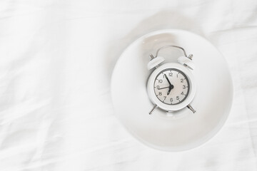 white alarm clock on plate with messy white bed sheet , early wake up , awaken  ,don't disturb , privacy or reminder  concept with copy space , panoramic