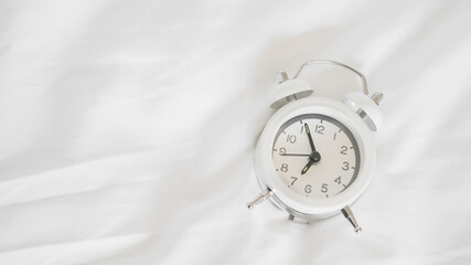 white alarm clock on messy white bed sheet , early wake up , awaken  or reminder concept with copy...