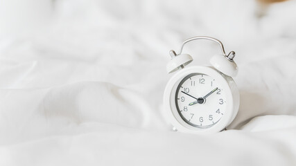 white alarm clock on messy white bed sheet , early wake up , awaken  or reminder concept with copy...
