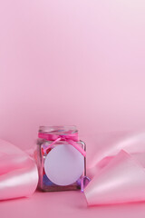 Obraz na płótnie Canvas Mockup with a place for a logo. Glass jar with hearts inside and a pink silk ribbon on a pink background. Concept for Valentine's Day. Template, banner. Vertical format. Copyspace