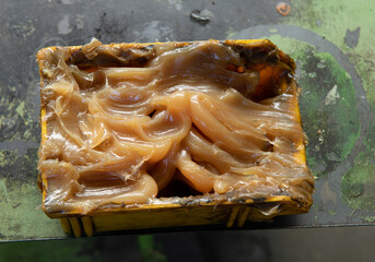 Yellow industrial grease in a plastic bowl on a metal plate.