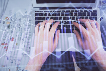 Double exposure of man's hands typing over laptop keyboard and forex chart hologram drawing. Top view. Financial markets concept.