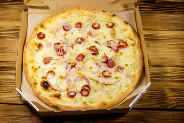 Delicious fresh pizza in cardboard box on a wooden table. Top view. Concept for home delivery of food, fast food, delivery of pizza