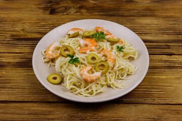 Spaghetti pasta with prawns, green olives and parsley on wooden table