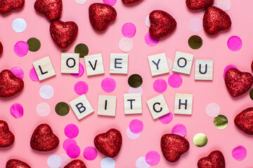 card for valentine's day. on a pink background wooden letters lined with love you bitch. funny congratulations. Flat lay, top view