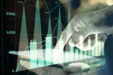 Double exposure of man's hands holding and using a digital device and forex graph drawing. Financial market concept.