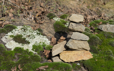 Stacked natural stones in balance in a landscape with rocks overgrown with fresh green moss