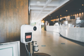 white digital Infrared thermometer   for check temperature measurement screening from COVID-19 for check in  hotel's lobby or building , in soft focus with blurred alcohol bottle