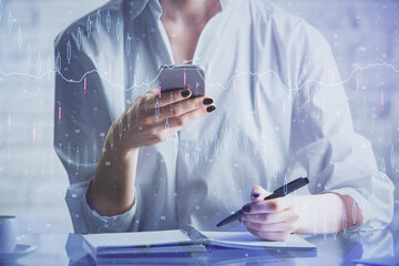 Double exposure of financial graph sketch hologram and woman holding and using a mobile device. Stock exchange concept.