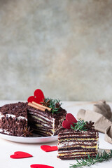 The piece of chocolate layered cake and red hearts on light concrete background. Festive Valentines Day decor. Russian honey cake, Medovik.
