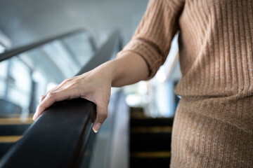 Hand of young woman touching the escalator during Coronavirus pandemic,risk of contagious or contamination of COVID-19,virus,bacteria or germs avoid touching handrail of escalator in public places - obrazy, fototapety, plakaty