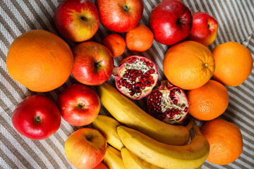 Ripe tangerines, oranges, apples and bananas lie on a gray mottled canvas. A pomegranates is torn in half in the middle. Horizontal photo.
