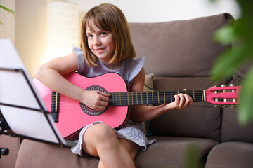 Girl practicing guitar sitting on sofa at home looking sideways