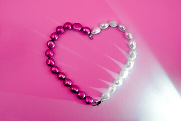 Pearl beads as heart on a pink background with light effect.