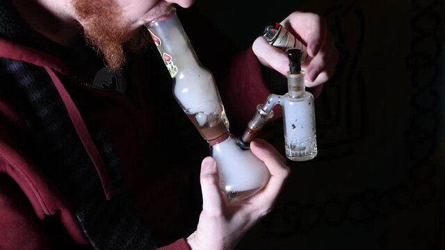 Slow motion use of a glass pipe bong. Inhale to bubble base then bowl is pulled from downstem to allow smoke to flow through. Exhale of smoke follows