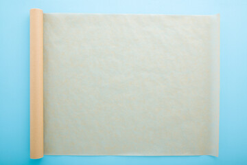 Rolled out roll of baking paper on light blue table background. Pastel color. Closeup. Empty place...