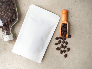 White paper bag with zipper and coffee beans in a bottle, wooden scoop on a grey background. Top...