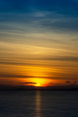 Silhouette mountain with sun and line clouds in sunset sky.