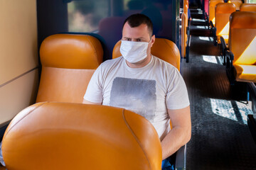 Serious young man looking at window wearing face protective mask in train to protect the respiratory system from coronavirus infection, covid-19. Preventive measure. Empty transport. 