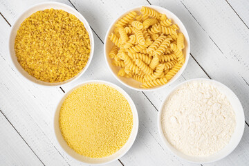 Flour, koukous, bulgur and pasta in bowl on wood table, top view. Various wheat products concept.