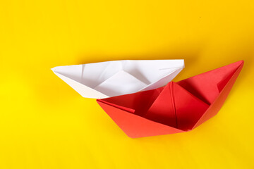 White and red paper ship isolated on yellow background. Origami boats. Concept of tolerance for differences