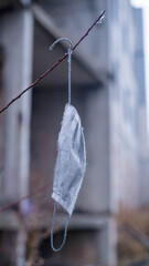 a used coronavirus mask hangs on a branch against the backdrop of a destroyed building