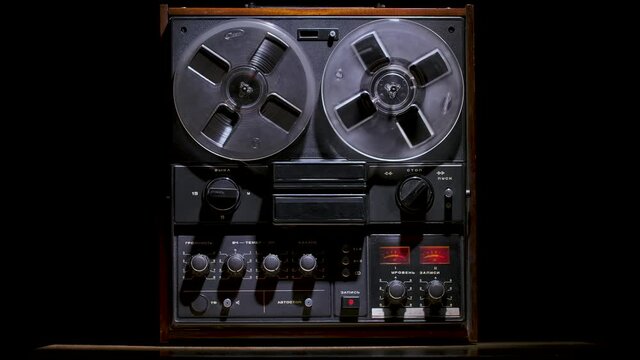 Male hands run vintage reel to reel tape recorder against a black studio background. Retro analogue music player. Front view close up. Popular disco trends 70s, 80s. Slow motion.