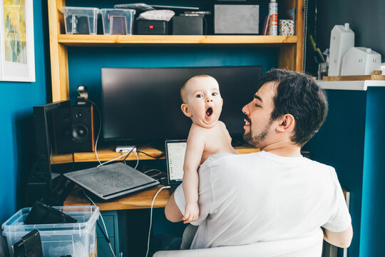 Father working from home alone, feeding his daughter in front of desk with computer. Stay home, quarantine remote work.