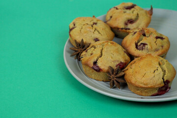 a star of brown anise and five muffins made from rice flour, yogurt, cherries and pumpkin oil lie on a gray plate on a turquoise background on the side. gluten-free homemade cakes