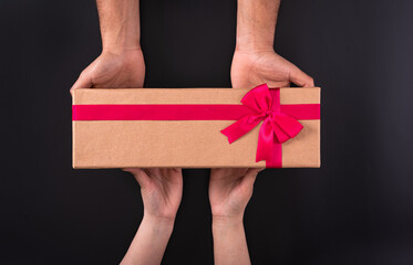 A person giving light brown color box in hands along with red color ribbon to a woman.
