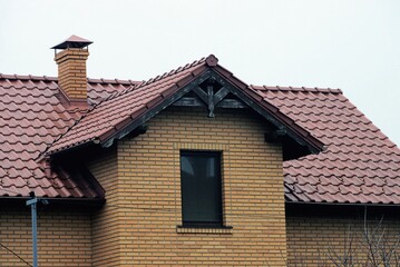 attic of a brown brick private house with a  window under a tiled roof against a gray sky