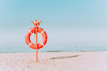 red lifebuoy on a sandy beach in pastel colors. Red lifebuoy on the sandy shore of the beach on a sunny day against the background of blue water