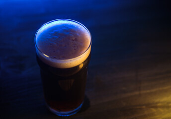 A glass of dark stout or porter beer on a wooden table, neon lighting and copy space