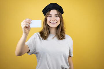 Beautiful young caucasian girl wearing french look with beret over isolated yellow background smiling and holding white card