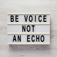 'Be voice not an echo' on a lightbox on a white wooden background, top view. Flat lay, overhead, from above.