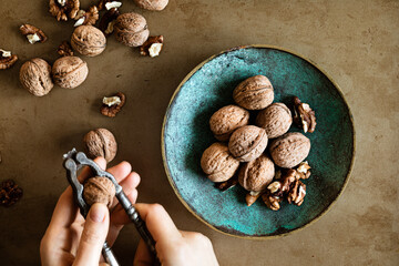Woman's hands peeling walnuts with a nutcracker on a table, overhead view