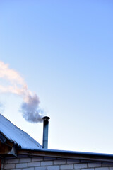 Iron chimney with smoke on the roof in winter