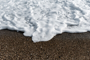 White sea foam on multi-colored pebbles. Close up.