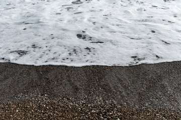 White sea foam on multi-colored pebbles. Close up.