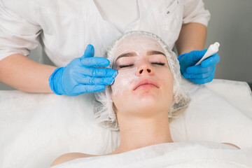 Obraz na płótnie Canvas Treatment, cure of face skin in cosmetology clinic. Beauty procedure with problem skin for young woman. Cosmetologist doctor is applying cream with anesthesia before PRP therapy procedure.