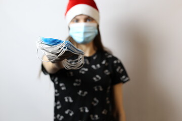 A girl in a Santa hat and white gloves holds many medical masks in her hands