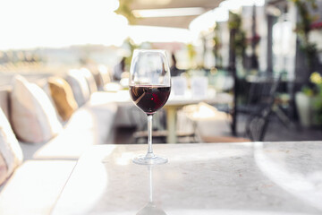 A glass of red wine on a marble table. Rooftop terrace, cosy lounge restaurant with couch and pillows