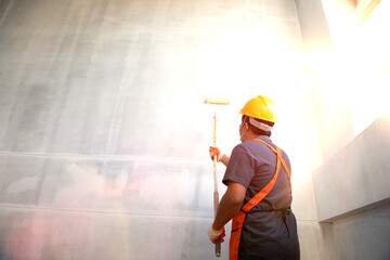 Room paint job. Asian white room painter with a paint roller in a great hall on a construction site.