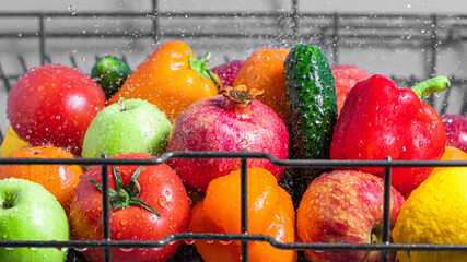 Vegetables and fruits are washed with water in the dishwasher basket close-up, water splashes.