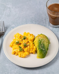 Keto diet breakfast scrambled eggs and avocado with olive oil and a cup of coffee over a clear grey background.