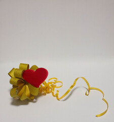 A large golden bow, near which lies a red heart on a white background.