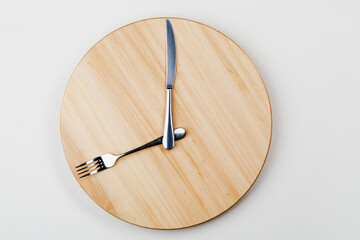 The concept of intermittent fasting and skipping meals. Wooden round tray with Cutlery in the form of clock hands. The concept of the eight-hour window of feeding or the concept of Breakfast time.