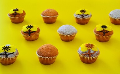 Rows of muffins decorated with powdered sugar and yellow flower shaped icing on a yellow background