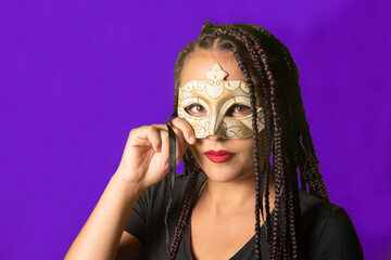 Fototapeta na wymiar Beautiful girl with braids in her hair and carnival mask, colorful background, selective focus.