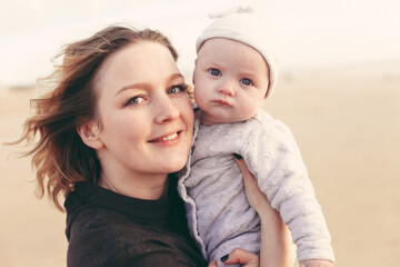 A young happy mother and a baby n a hat, looking at the camera, outdoors